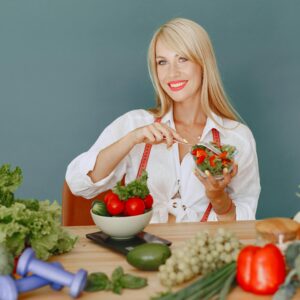 Blonde woman enjoying a fresh salad surrounded by vegetables, promoting healthy eating.