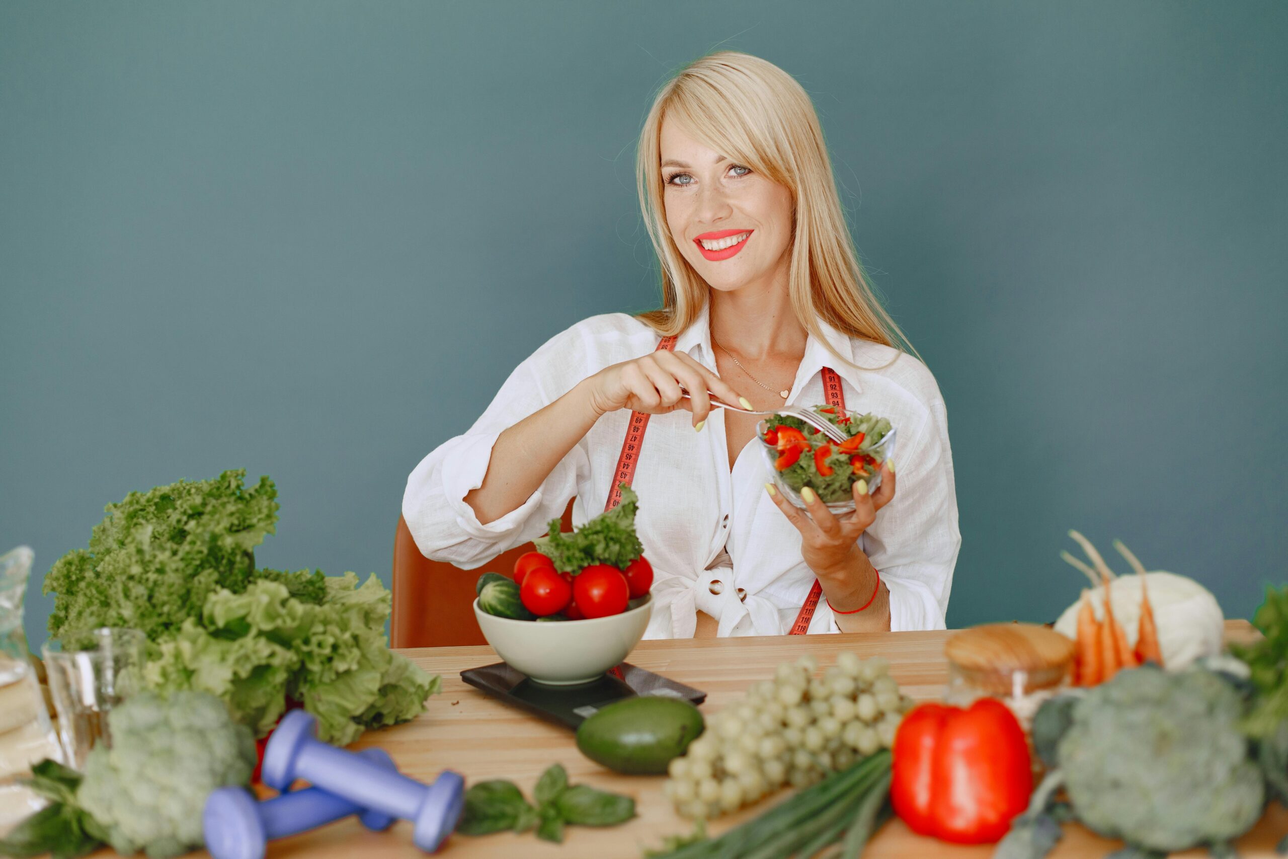 Blonde woman enjoying a fresh salad surrounded by vegetables, promoting healthy eating.