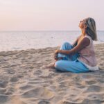 A peaceful moment as a woman relaxes on a sandy beach, enjoying the sunset.