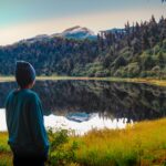 A serene landscape with a lone person by a reflective lake in Mérida, Venezuela, surrounded by vibrant forests.